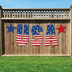 an american flag banner hanging on a fence in front of a wooden fence with grass