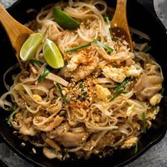 a bowl filled with noodles and chicken on top of a wooden spoon next to lime wedges