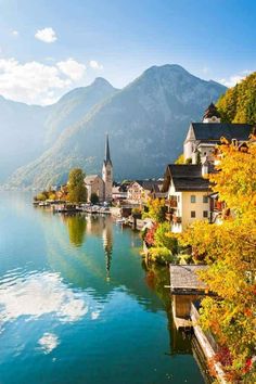 a lake surrounded by mountains with houses on the shore and trees in front of it