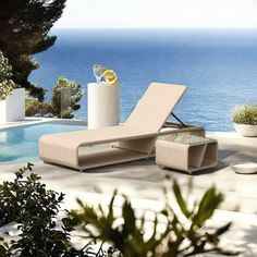 an outdoor lounge chair next to a swimming pool and ocean in the background with plants