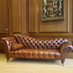 a brown leather couch sitting in front of a wooden paneled wall with paintings on it