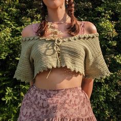 a woman wearing a crop top and skirt in front of some bushes with her hands on her hips