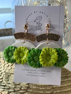 two green and yellow flower earrings are on top of a card with a price tag