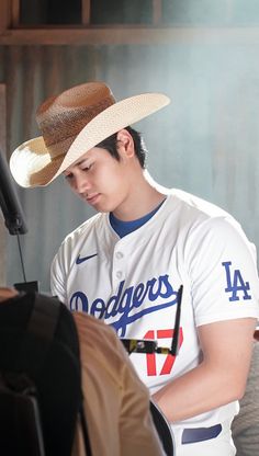 a baseball player wearing a hat and looking at his cell phone in the dugout