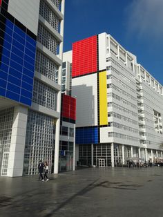 the building is multicolored and has people walking in front of it on a sunny day