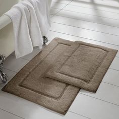 two bath mats sitting next to each other on the floor in front of a tub