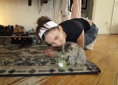 a woman is laying on the floor with her cat and drinking from a cup while looking at the camera