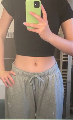 a woman in grey sweat pants holding a green cell phone and looking at her stomach