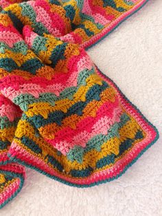 a colorful crocheted blanket laying on top of a white bed next to a pair of slippers