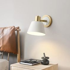 a bedside table with a lamp on it next to a book and pillow in a bedroom