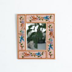 a mirror that is on the wall with flowers and birds painted on it's sides