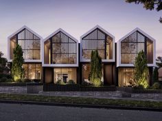 an artist's rendering of three modern houses in the evening with trees and bushes