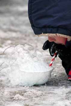 a young boy is drinking from a bowl filled with ice and water, while holding a red and white striped straw