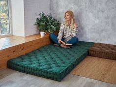 a woman sitting on top of a green mattress in front of a window with potted plant