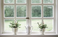 three white vases with flowers sit on a window sill