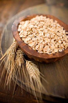 a wooden bowl filled with oatmeal on top of a table next to wheat stalks