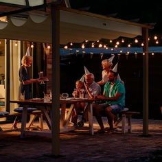 some people sitting at a picnic table with lights strung over the top and around them