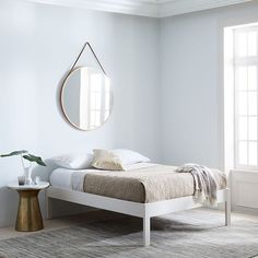 a white bed sitting in a bedroom next to a round mirror on the side of a wall