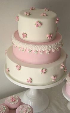 a three tiered cake with pink frosting and flowers on the top is surrounded by cupcakes