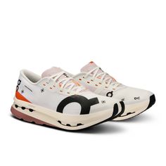 a pair of white sneakers with black and orange details on the upper part of the shoe