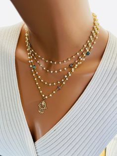 This is a gorgeous 14 karat gold filled multi strand pearl necklace. This necklace features a 14 karat gold filled Hamsa pendant that measures 22X 18 MM. Pearls measure 3 to 3.5 MM. Beautiful colorful Marano glass Evil eye connectors are scattered on this necklace. Spring clasp in back connects all four strands. This necklace is much more stunning in person. Model is wearing the 15 to 18 inch length. Longer lengths available and drop-down list. This necklace may also be ordered in 925 sterling silver version, not shown. Comes in a gift box ready to present. Elegant Gold Evil Eye Necklaces, Elegant Gold Evil Eye Necklace, Gold Multi-strand Pearl Charm Necklace, Gold Multi-strand Necklace With Pearl Charm, Elegant Gold Plated Evil Eye Charm Necklace, Multi-strand Pearl Drop Jewelry As Gift, Pearl Drop Multi-strand Jewelry Gift, Multi-strand Pearl Drop Jewelry Gift, Gold Multi-strand Spiritual Jewelry