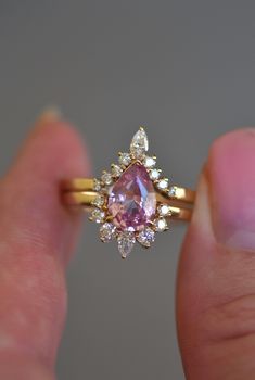 a woman's hand holding an engagement ring with a pink diamond in the middle