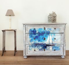 a blue and white painted dresser sitting next to a lamp on a wooden floor in front of a wall