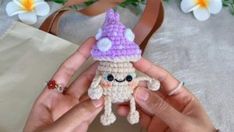 a hand holding a small crocheted toy with a purple hat on it's head