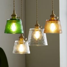 three different colored glass lights hanging from a light fixture in a kitchen or dining room