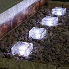 some ice cubes that are sitting on some rocks and gravel in front of a brick wall