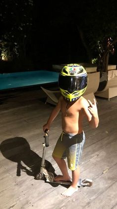 a young boy wearing a helmet and holding a scooter in front of a swimming pool