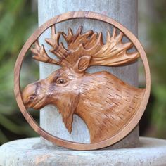 a wood carving of a moose head in a circle on a pillar with trees behind it