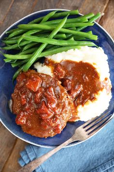 two meatballs covered in gravy and green beans on a plate with mashed potatoes