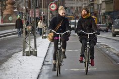 two women riding bikes down a snowy street