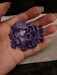 a person's hand holding a purple and black brooch with an image of a woman on it