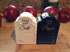 two salt and pepper shakers sitting on top of a wooden table next to apples