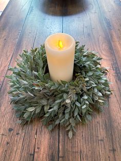 a lit candle sitting on top of a wooden table next to a wreath with leaves