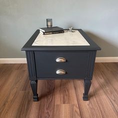 a small black table with two drawers and a white marble top on wooden flooring