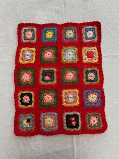 a red crocheted square with many squares on it, sitting on a white surface