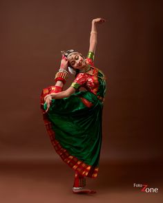 a woman in a green and red sari dancing with her arms up to the side