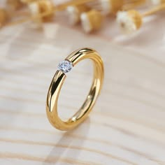 a yellow gold ring with a single diamond on the side, sitting on a white background