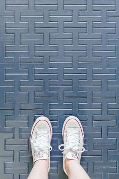 a person wearing white tennis shoes standing in front of a blue wall