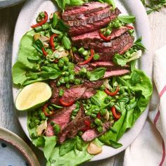 steak salad with red peppers and green onions on a white plate next to a glass of orange juice