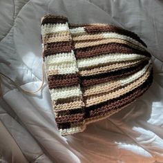 a crocheted hat is laying on a bed with white sheets and brown trim