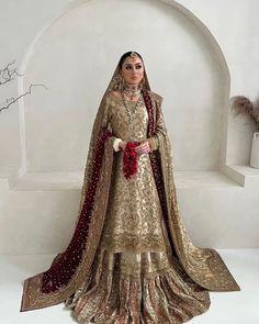 a woman in a gold and red wedding dress standing next to a white wall with an arch