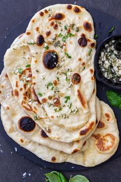 several flat breads with olives and parsley on a black plate next to a bowl of feta cheese