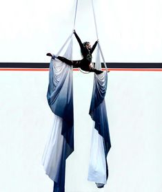 a woman hanging upside down in the air with her arms and legs wrapped around two pieces of fabric