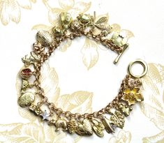 Beautiful vintage inspired bracelet with 24 mixed theme brass charms on a brass belcher chain. The charms are all 3d and include 3 workable lockets and 6 rhinestone embellished ones. There is also a  lion, cowboy hat, theatre mask, pair of dice, hare, turtle, teapot, snail, sandals, teddy bear, crab, compass, dragonfly, bear, star, lantern, fruits flowers, and foliage.  The bracelet is polished to a lovely golden colour and sealed with numerous coats of wax though as with all brass jewellery it will darken with time but can be repolished or left to form a natural patina as desired. The bracelet will be supplied in a velvet gift pouch. Vintage Charm Brass Bracelet, Vintage Gold Charm Bracelet With Dangling Charms, Antique Gold Charms With Dangling Details, Gold Brass Charm Bracelet With Vintage Charm, Vintage Gold Bracelets With Charms, Vintage Gold Jewelry With Removable Charms, Gold Vintage Bracelets With Charms, Vintage Charm Bracelet With Removable Charms, Vintage Charm Bracelet With Removable Charms As Gift