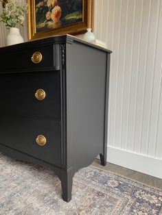 a black dresser with gold handles and knobs in a room next to a painting on the wall