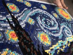 a person is holding up a crocheted blanket